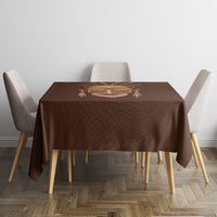 Brown tribal tablecloth with mask motif on square table, sides falling over chairs