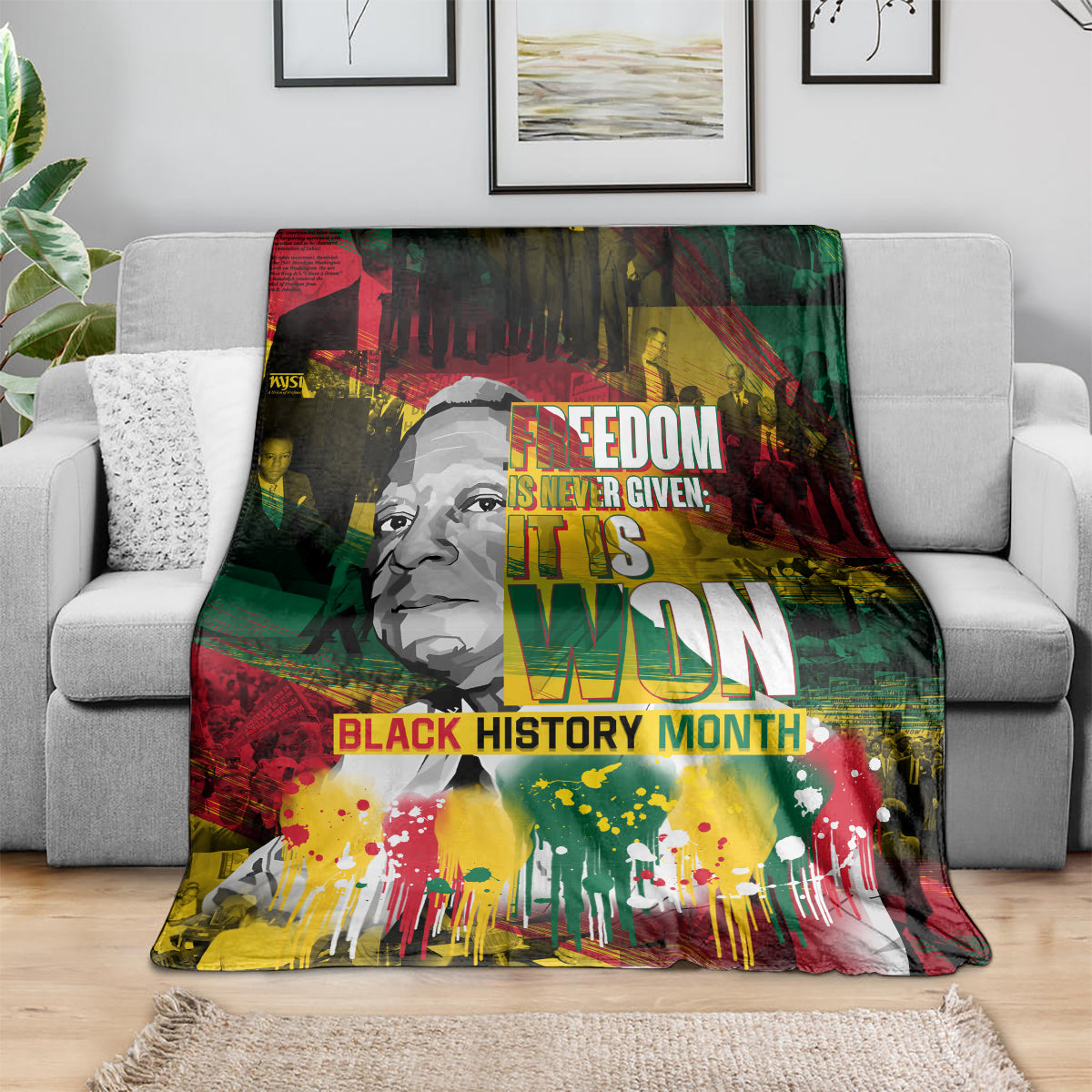 Black history portrait blanket draped on gray sofa, colorful splatter and large central lettering