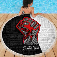 Round beach blanket laid on wood deck, black word background with red justice-fist motif and fringe