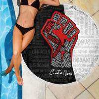 Round beach blanket with fringed edge by a pool, black-and-white text pattern with red justice fist
