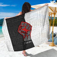 Black and light-gray sarong held open, featuring a red justice-fist emblem and text
