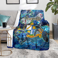 Blue Anguilla blanket on a chair, showing sea turtle and shell print with scalloped scales.