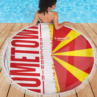 Round beach blanket with red and yellow flag design, white fringe border on wooden deck