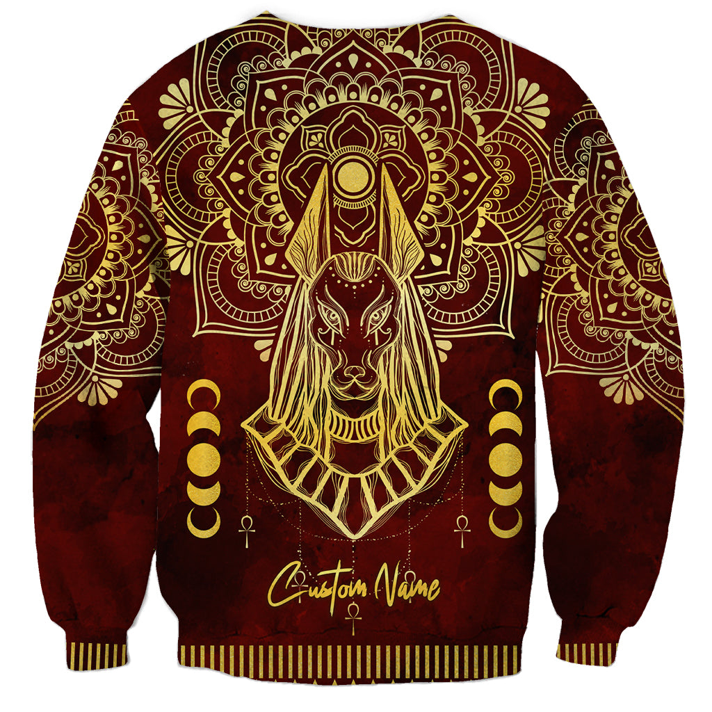 Red unisex sweatshirt with gold Anubis portrait, mandala pattern, and cursive text