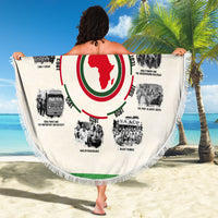 Beige round beach blanket held up, featuring African timeline ring and red/green center, fringe