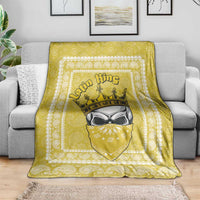 Yellow paisley throw blanket with centered crowned face design on a gray sofa