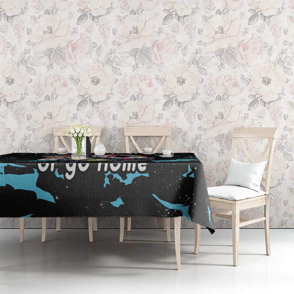 Black dinosaur unicorn tablecloth with blue splash pattern on dining table against floral wall.