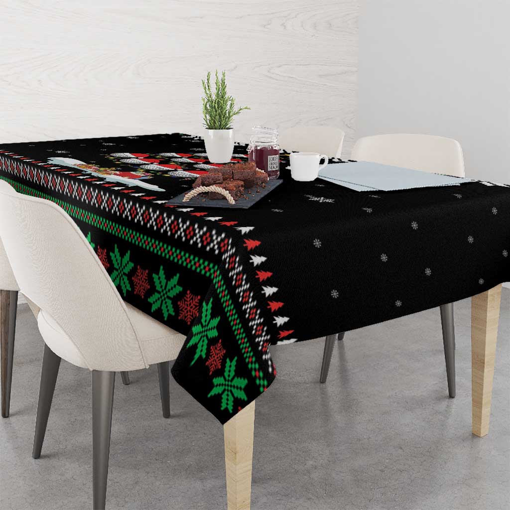 Black Christmas tablecloth draped over table with green holiday motif and red accents
