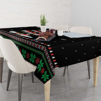 Black Christmas tablecloth draped over table with green holiday motif and red accents