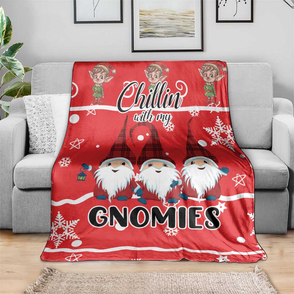 Red gnomies Christmas blanket draped on a gray sofa, showing “GNOMIES” and snowflakes
