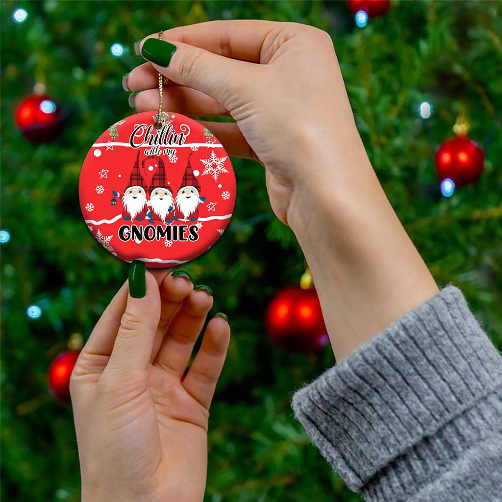 Red ceramic Christmas ornament with gnomes graphic, held by hand on a tree.