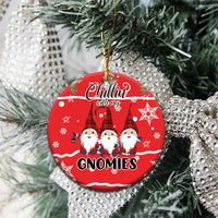 Red ceramic Christmas ornament with gnomes text design hanging on pine branches.