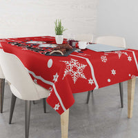 Red tablecloth with white Santa hat gnome graphic, stars, and snowflakes on dining table.