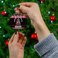 Black round ceramic Christmas ornament with Flamingo Humans graphic; gold loop; held by hand