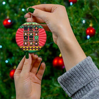Ceramic nutcracker ornament held in hands, red circular design and gold hanging loop