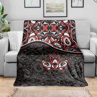 Black blanket laid on gray sofa with red and white Haida-style tribal pattern and maple leaf motif