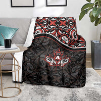 Black blanket draped over chair with red and white Haida-style tribal pattern and maple leaf motif