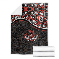 Folded black blanket with red and white Haida-style tribal pattern and maple leaf motif
