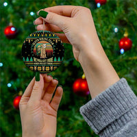 Black ceramic ornament with sloth hiking team graphic and gold hanging string, held by hands.