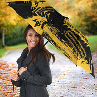 Black umbrella with bold yellow military graphic, person smiling while holding handle