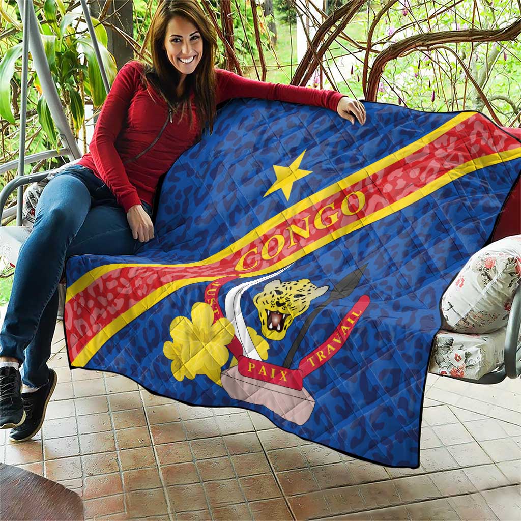 Blue quilted Congo flag blanket held outdoors, showing leopard emblem and yellow flower patch.
