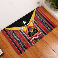 Rubber doormat corner view with black background, red stripes, yellow diagonal band, crest