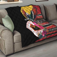 Black quilt draped on sofa with bird emblem, red-yellow wings, and geometric pattern