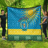Blue quilt blanket with Rwanda sun emblem held outdoors, yellow chevrons and green band