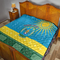 Blue quilt blanket on bed with sun emblem, yellow midstripe and green patterned edge