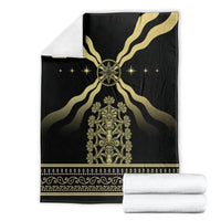 Black mythological spirit blanket with gold emblem, folded; white towels stacked beside