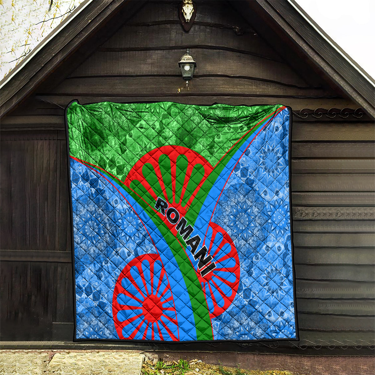 Romani quilt hanging on outdoor wall: green center stripe, blue patterned fabric, red wheels