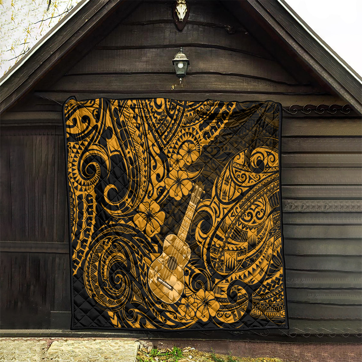Gold and black ukulele-themed quilt with Polynesian patterns, hanging on a wooden wall