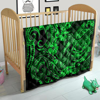 Green Polynesian fish-hook quilt covering a crib with clover and swirl motifs