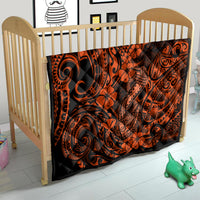 Orange and black Polynesian-pattern quilt on a baby bed, with swirl and flower details