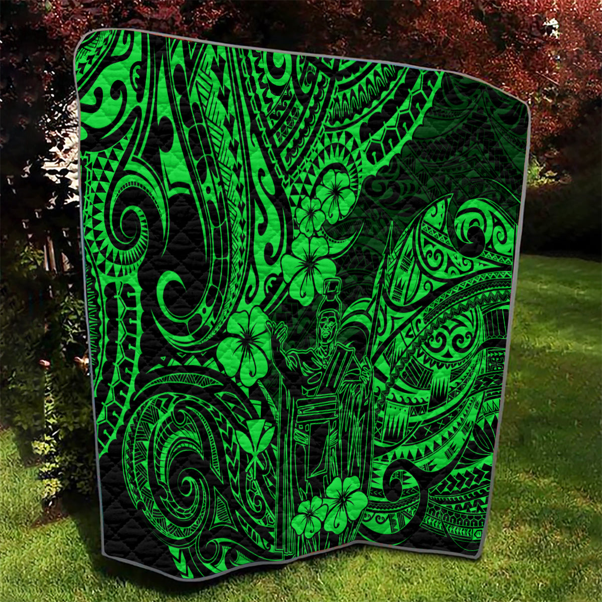 Green and black Polynesian pattern quilt laid on grass, full view