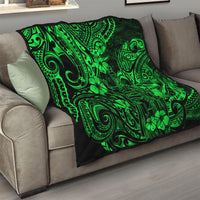 Green Polynesian pattern quilt folded over a gray sofa armrest