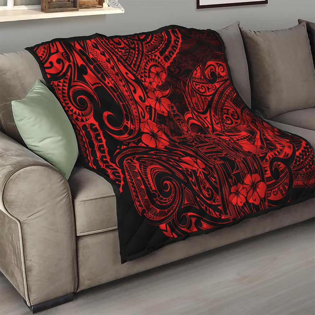 Red and black Polynesian patterned quilt with ornate tribal motifs, folded on sofa
