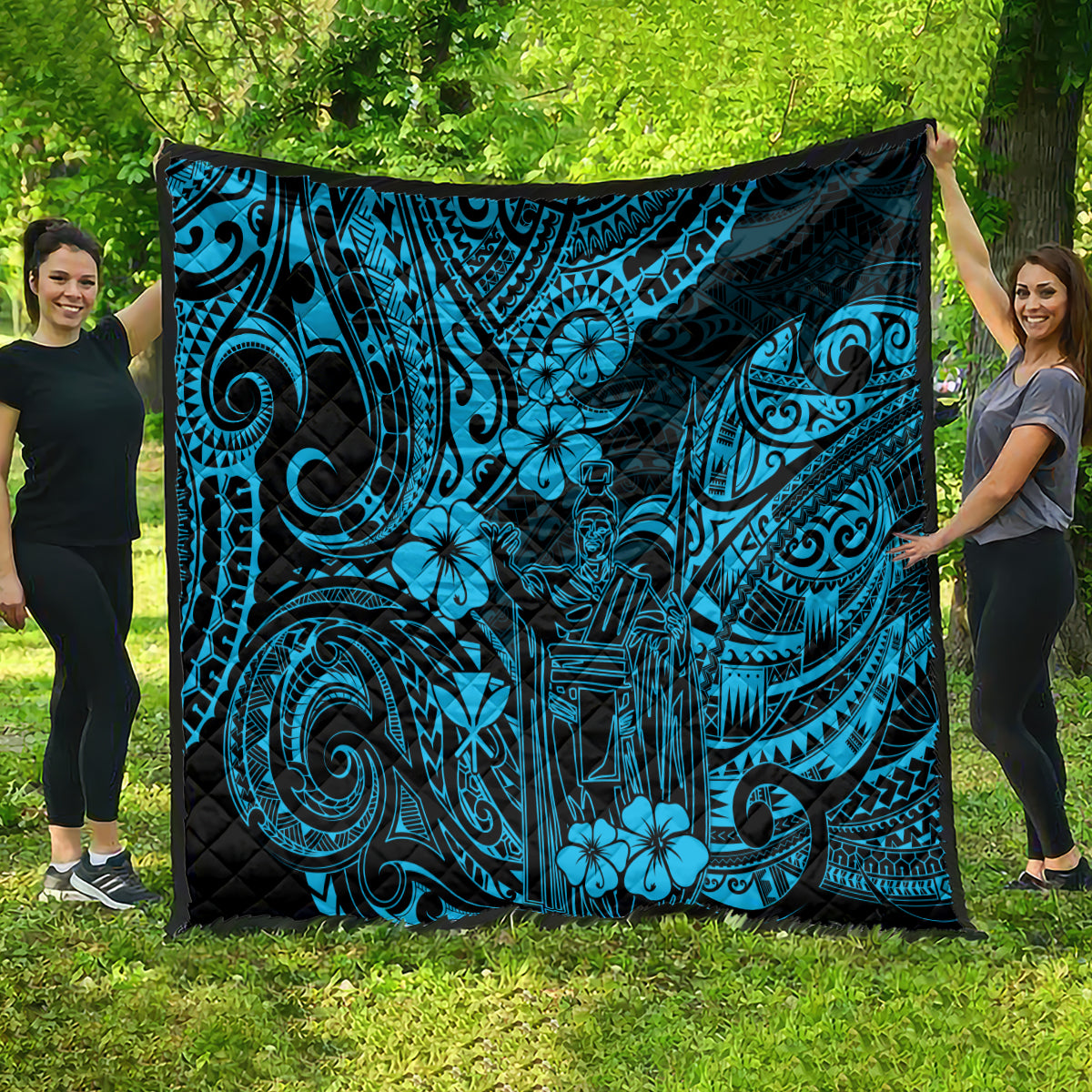 Blue Polynesian pattern quilt spread outdoors, with dark border and floral tiki designs.