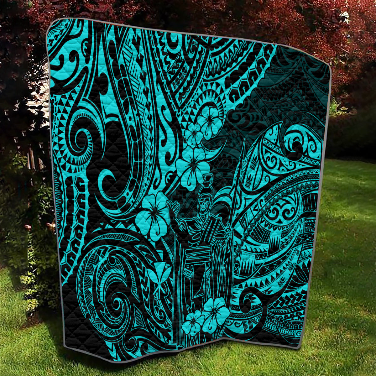 Turquoise Polynesian pattern quilt draped on lawn, black border and ornate icons