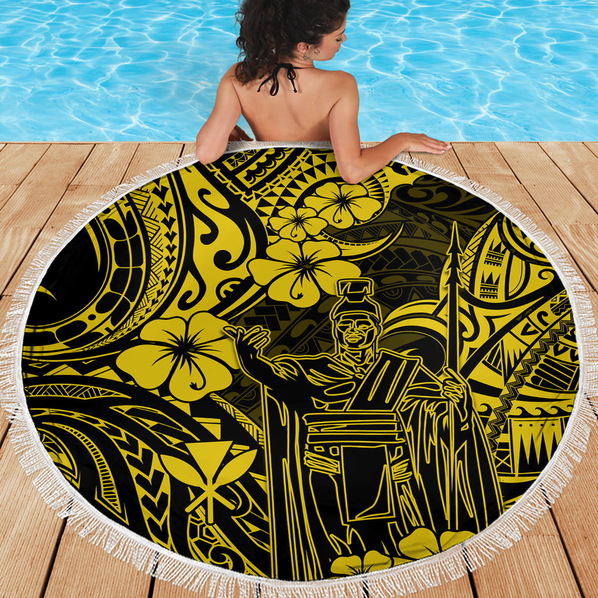Person draped in round beach blanket with yellow and black Polynesian pattern and white fringe.