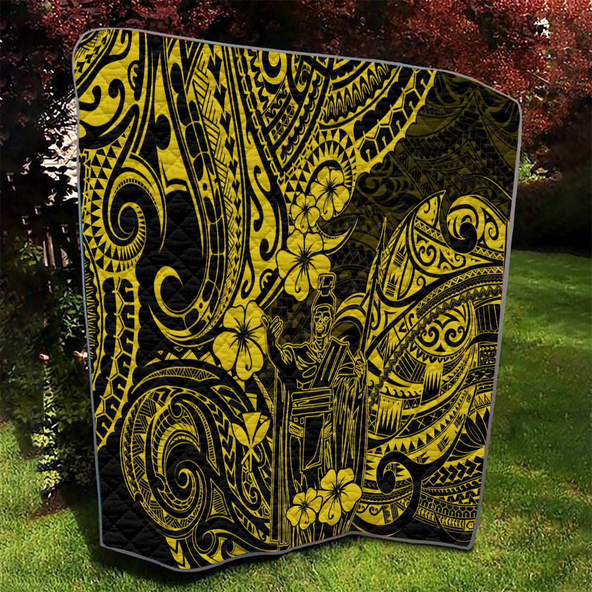 Yellow-and-black Polynesian pattern quilt draped over grass, corner visible