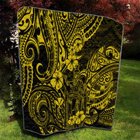 Yellow-and-black Polynesian pattern quilt draped over grass, corner visible