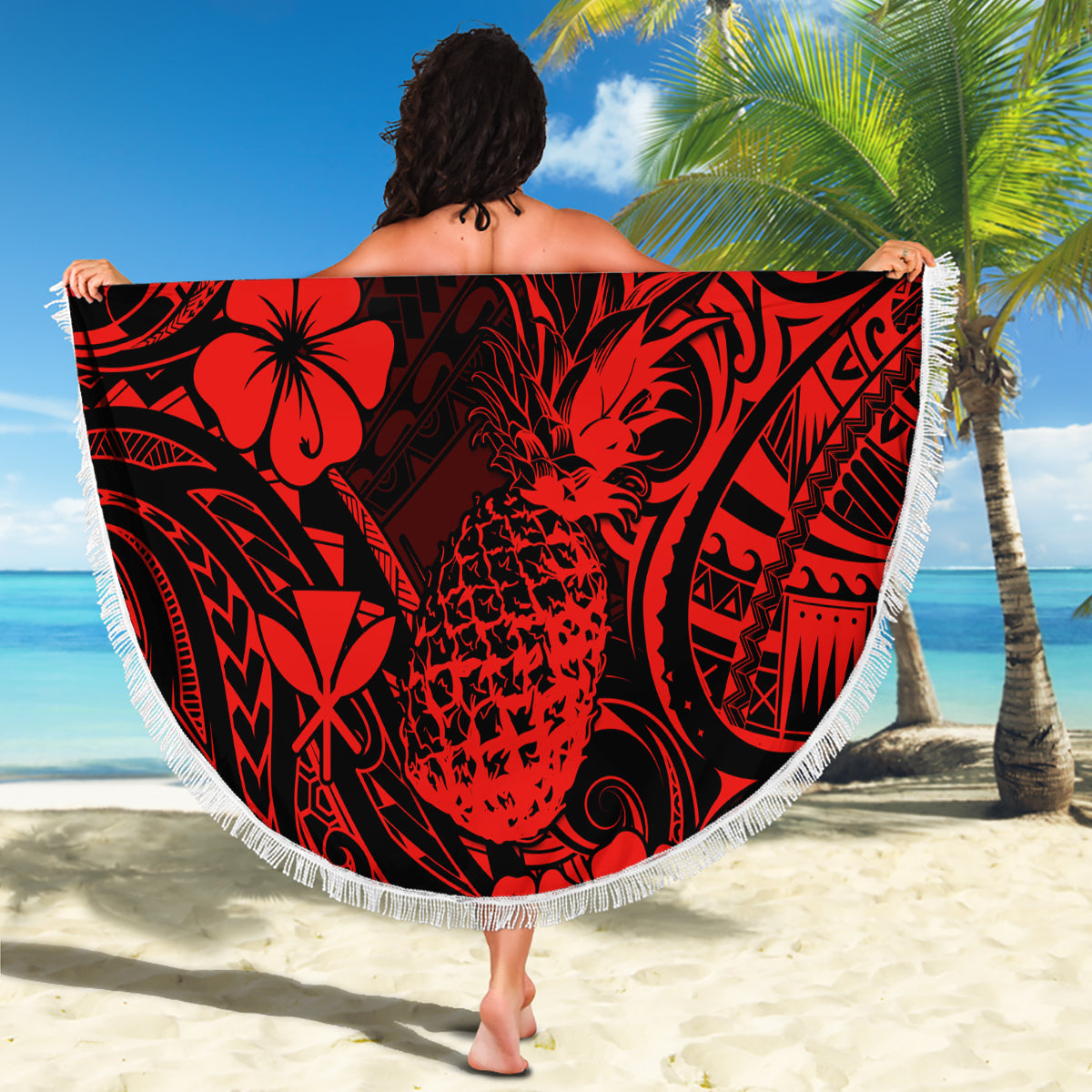 Red & black round beach blanket with white fringe, pineapple floral motif spread on sand