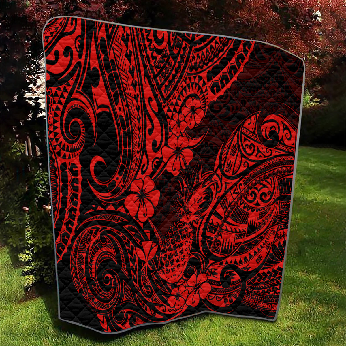 Red and black Polynesian pineapple quilt blanket draped on grass with curved swirl patterns
