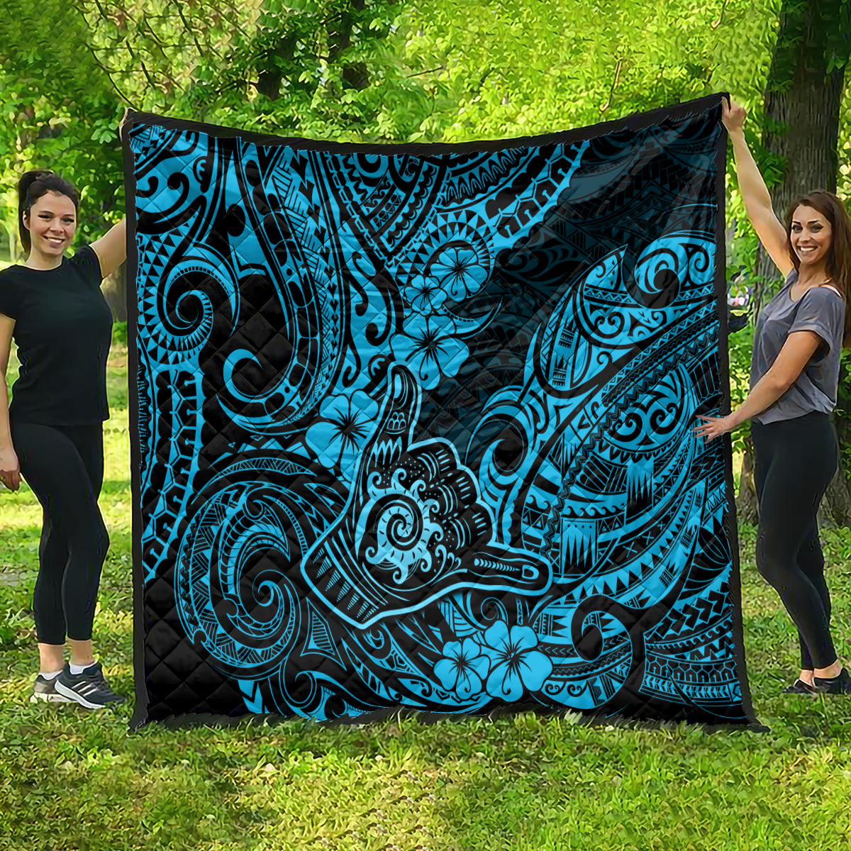 Blue Polynesian shaka pattern quilt with black backing, spread on green lawn