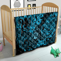 Blue Polynesian shaka pattern quilt with black backing, laid in wooden baby crib