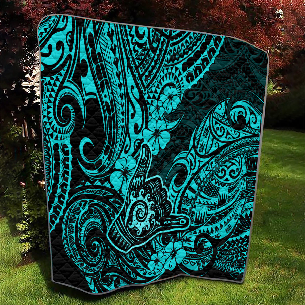 Turquoise Polynesian pattern quilt with black border laid on grass
