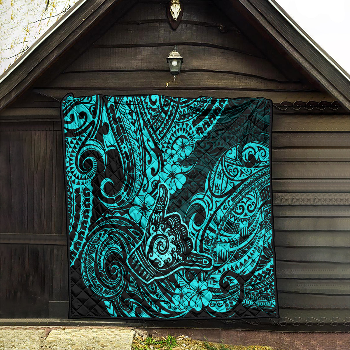 Turquoise Polynesian pattern quilt hanging indoors against dark wood wall