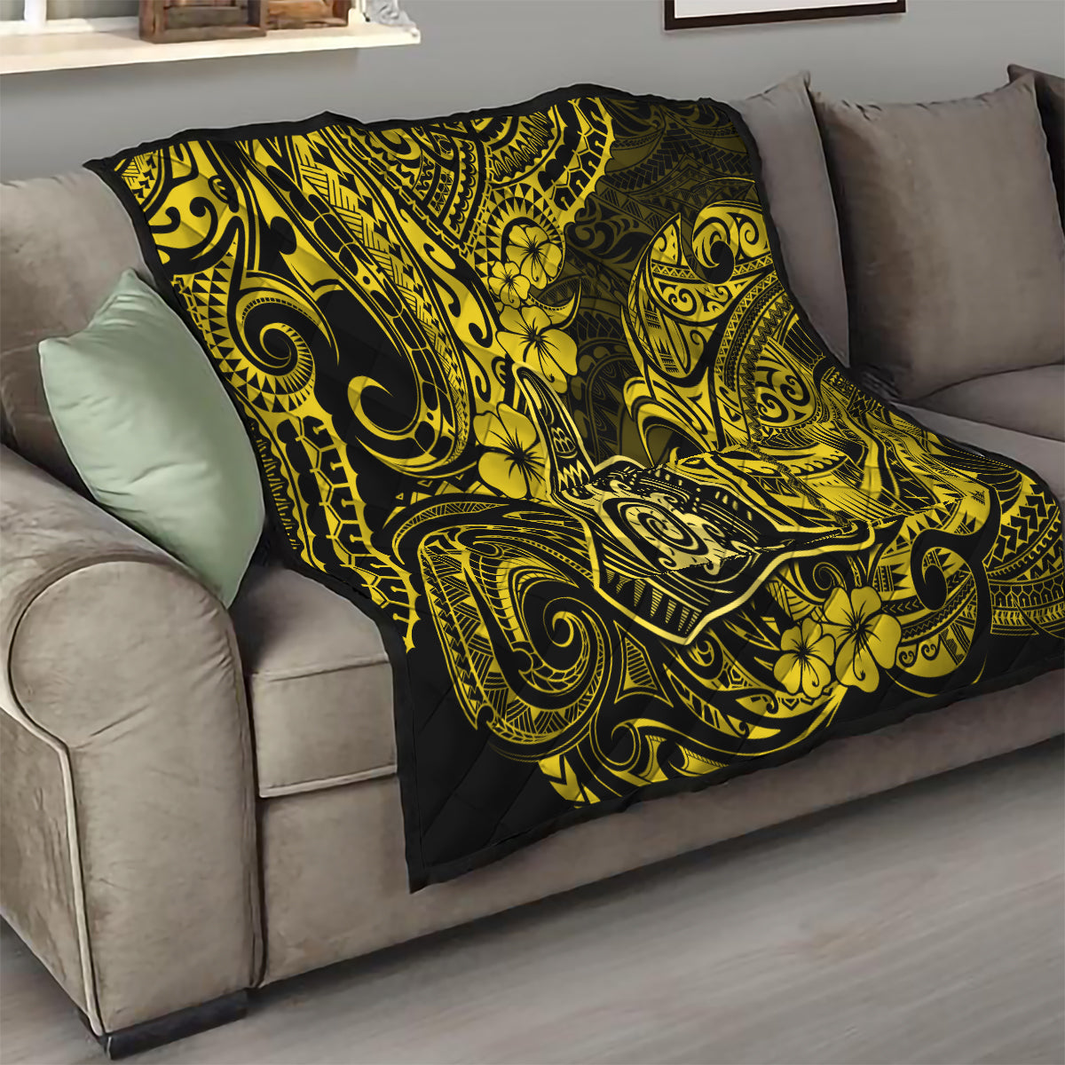 Polynesian shaka sign quilt draped on sofa, yellow and black with swirling floral motifs