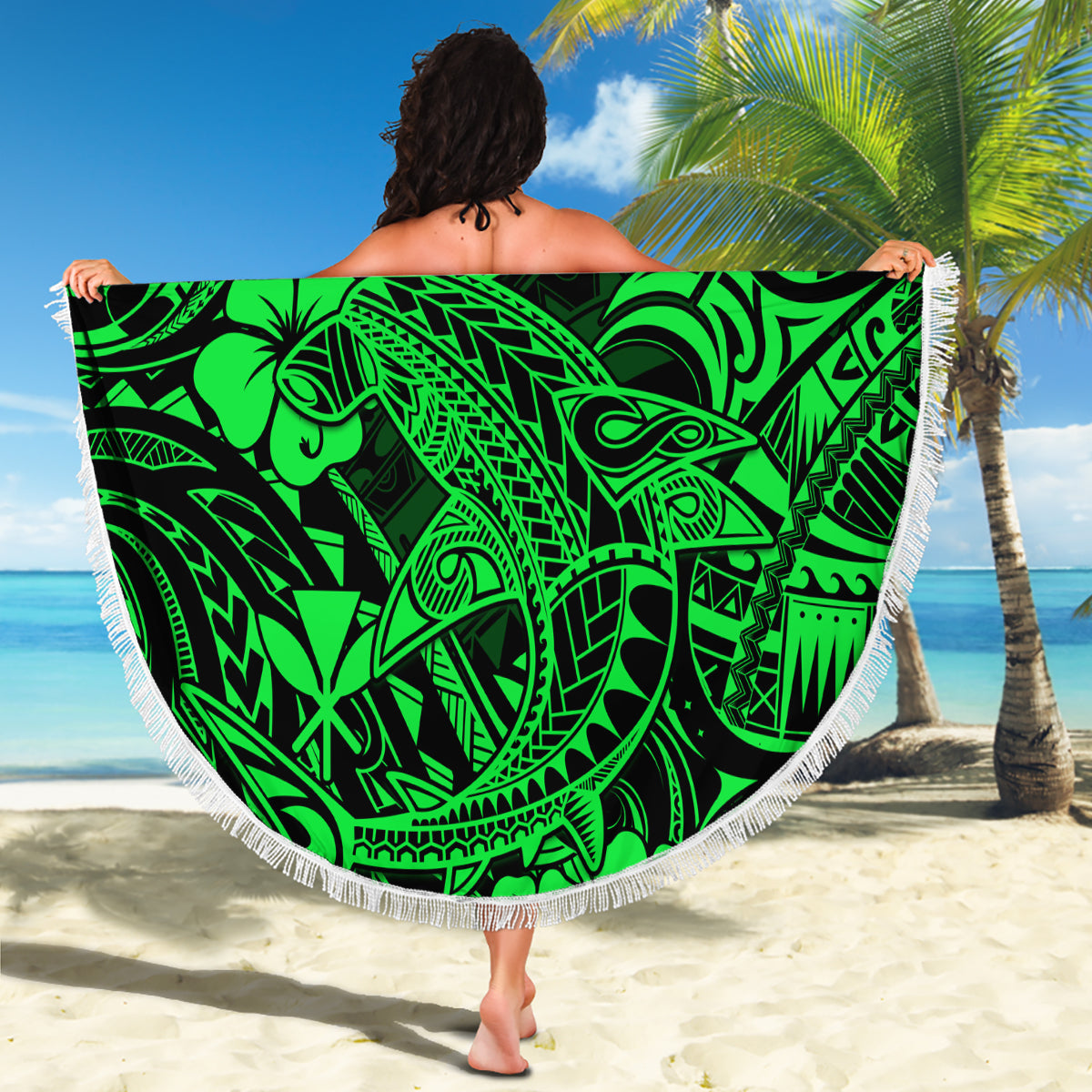 Green round beach blanket with white fringe, tribal shark design held on beach